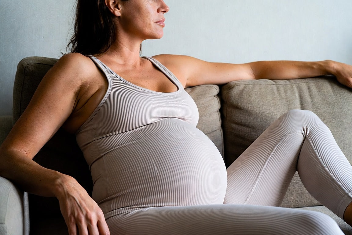 pregnant woman sitting in a sofa with a confident expression wearing a beige yoga jumpsuit