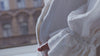 Zoomed in video of a pregnant woman wearing a white dress gently stroking her belly